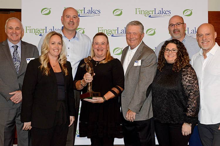 Distinguished Alumni Award winner with trophy in hand stands with FLCC staff.