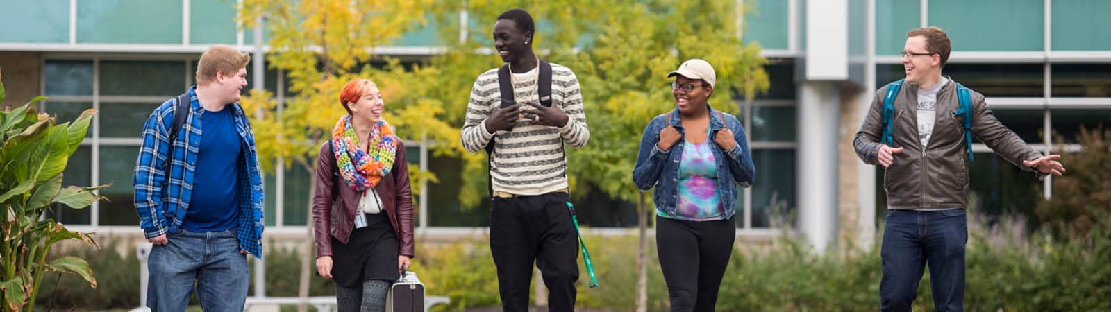 Five students walk in a group outside of FLCC main campus, talking and laughing.