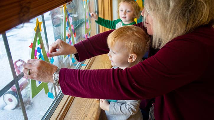 Preschool-age children hanging Christmas decorations on window.