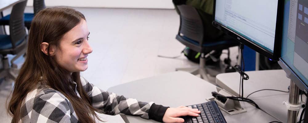 Computer Information Systems student coding in Java on a dual screen monitor