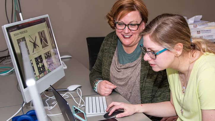 Graphic design faculty and student collaborating on a project in the Mac graphic design lab.