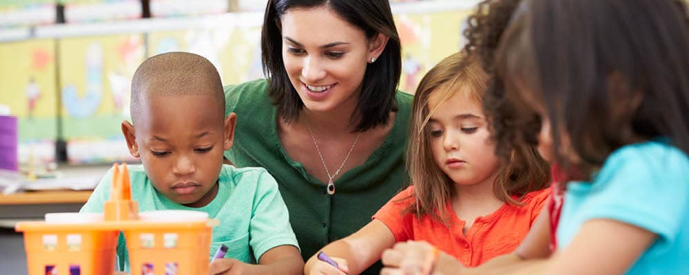 A teaching assistant helping 3 elementary students with an art project.